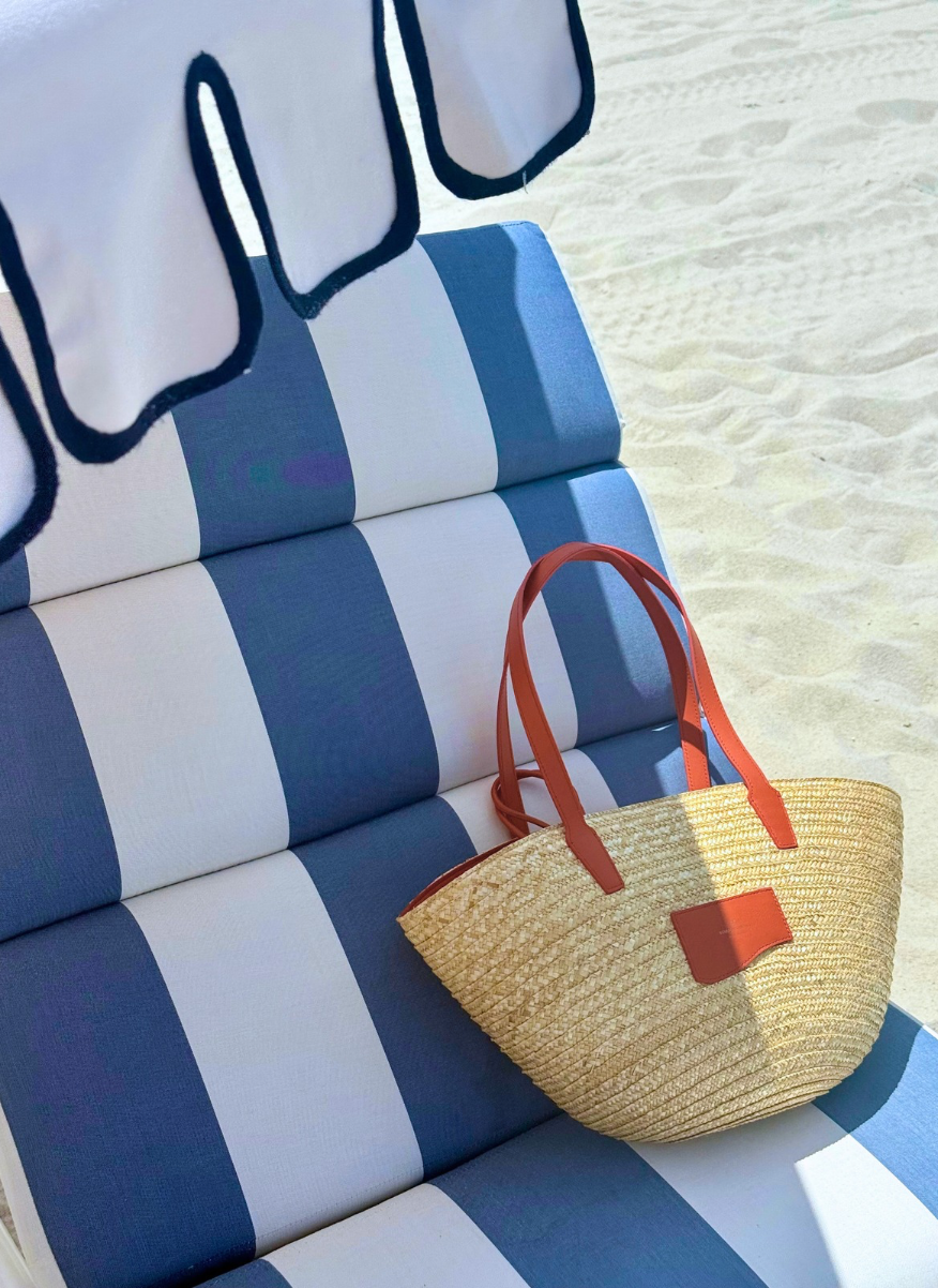 Lifestyle: Large Straw Marea Tote Bag, Orange Smooth Leather (Toasted Orange), bag laying on a beach chair. Miami Beach Scene.