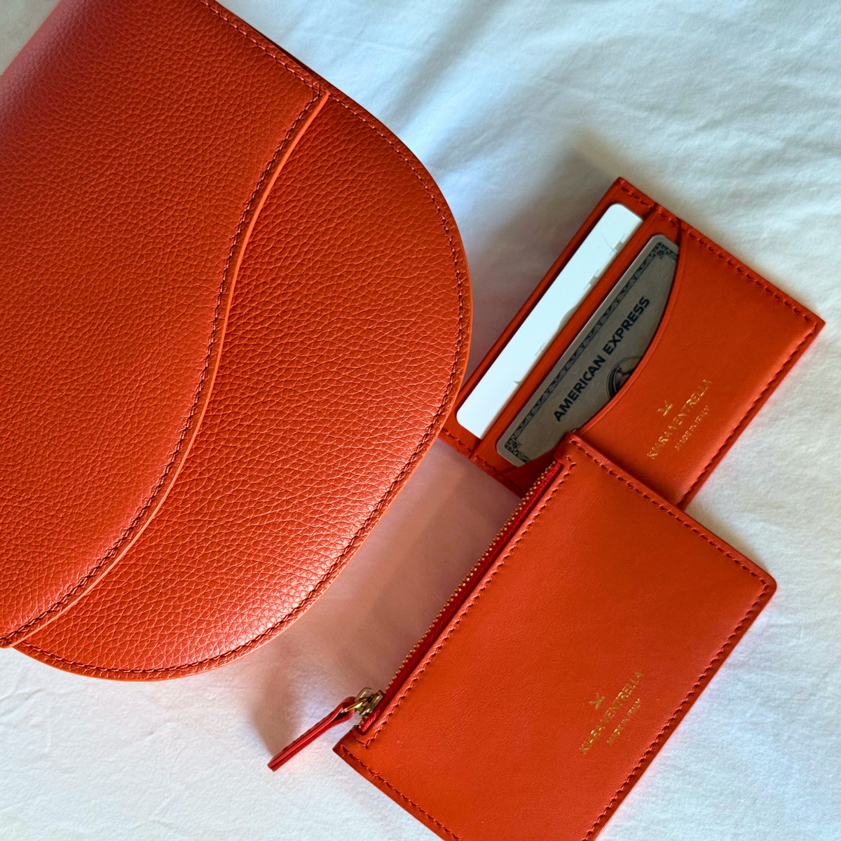 Lifestyle: Card Case Slim Smooth Orange leather. Matching Wave Saddle Bag and Extra Credit Cardholder (Toasted Orange). Matching small leather goods (SLG) Flat Lay.