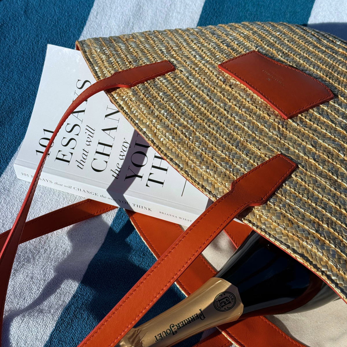 Lifestyle: Large Straw Marea Tote Bag in Smooth Orange leather (toasted orange), bag on beach chair. Size reference, inside view of bag, book and champagne.