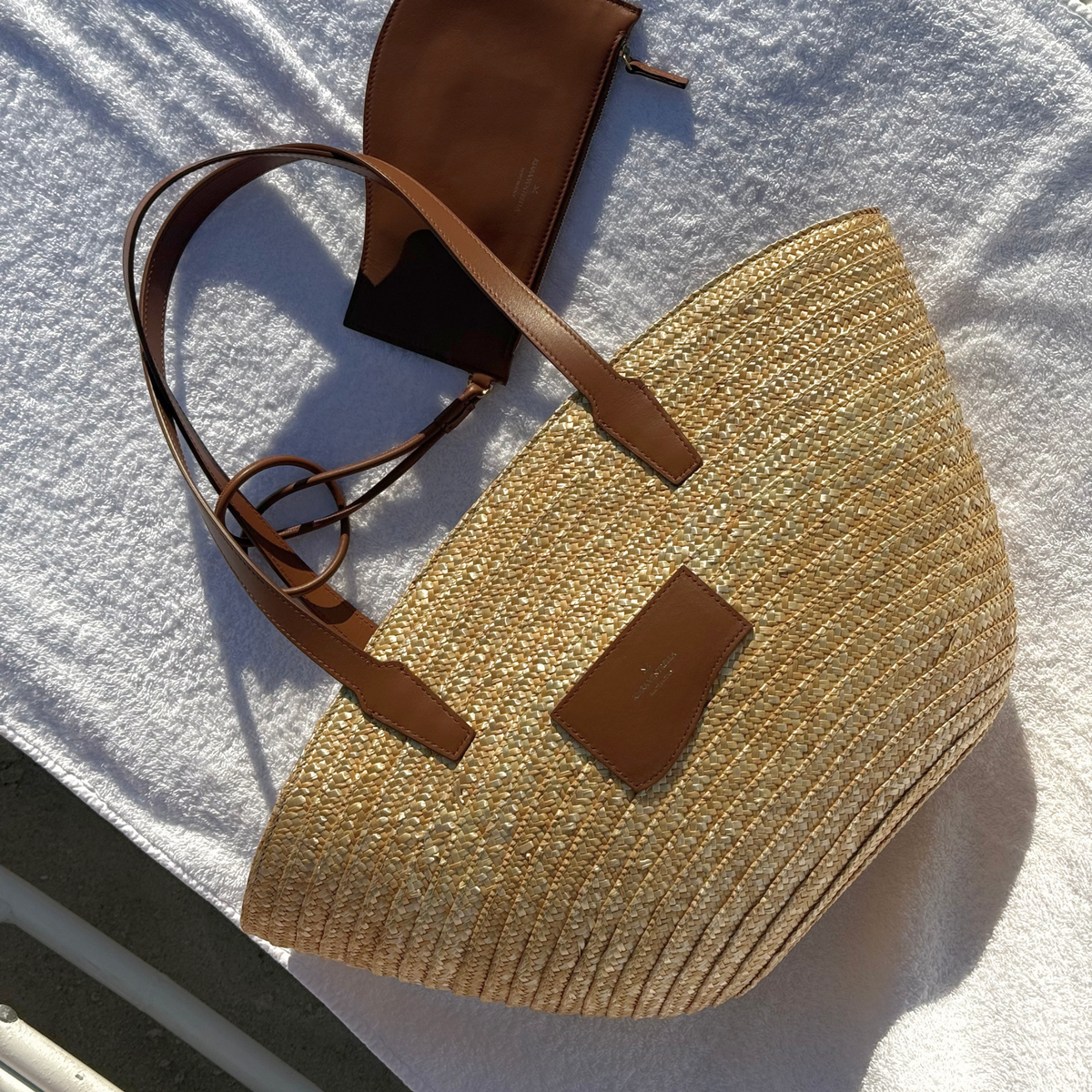 Lifestyle: Large Marea Straw Tote Bag with Marea Wave Pouch fastened to shoulder strap. Both shown in Chestnut Brown Smooth Leather.