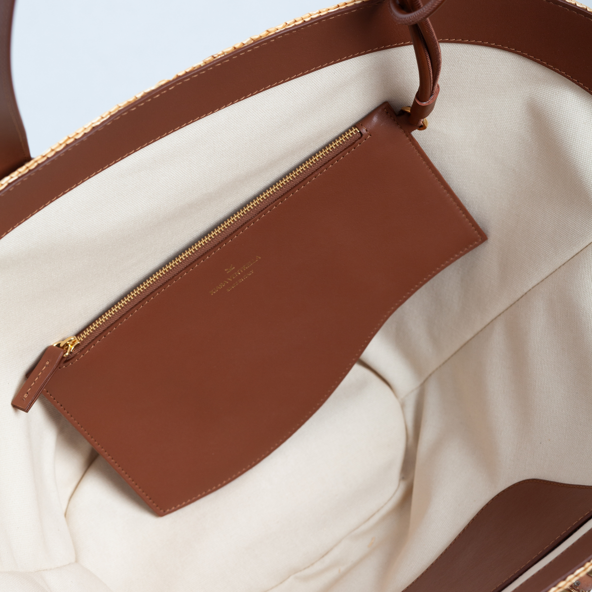 Marea Wave Pouch in Chestnut Brown leather, looped around to fasten to tote bag handle. Shown on Marea Large Straw Tote in Chestnut Brown.