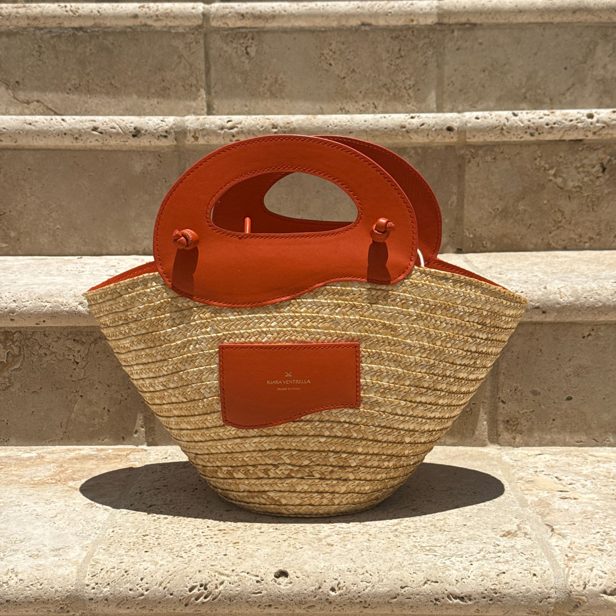 Lifestyle: Marea Straw Bag Small, Smooth Orange Leather (Toasted Orange),  Leather Wave handles. Lifestyle Outdoor Limestone Steps.