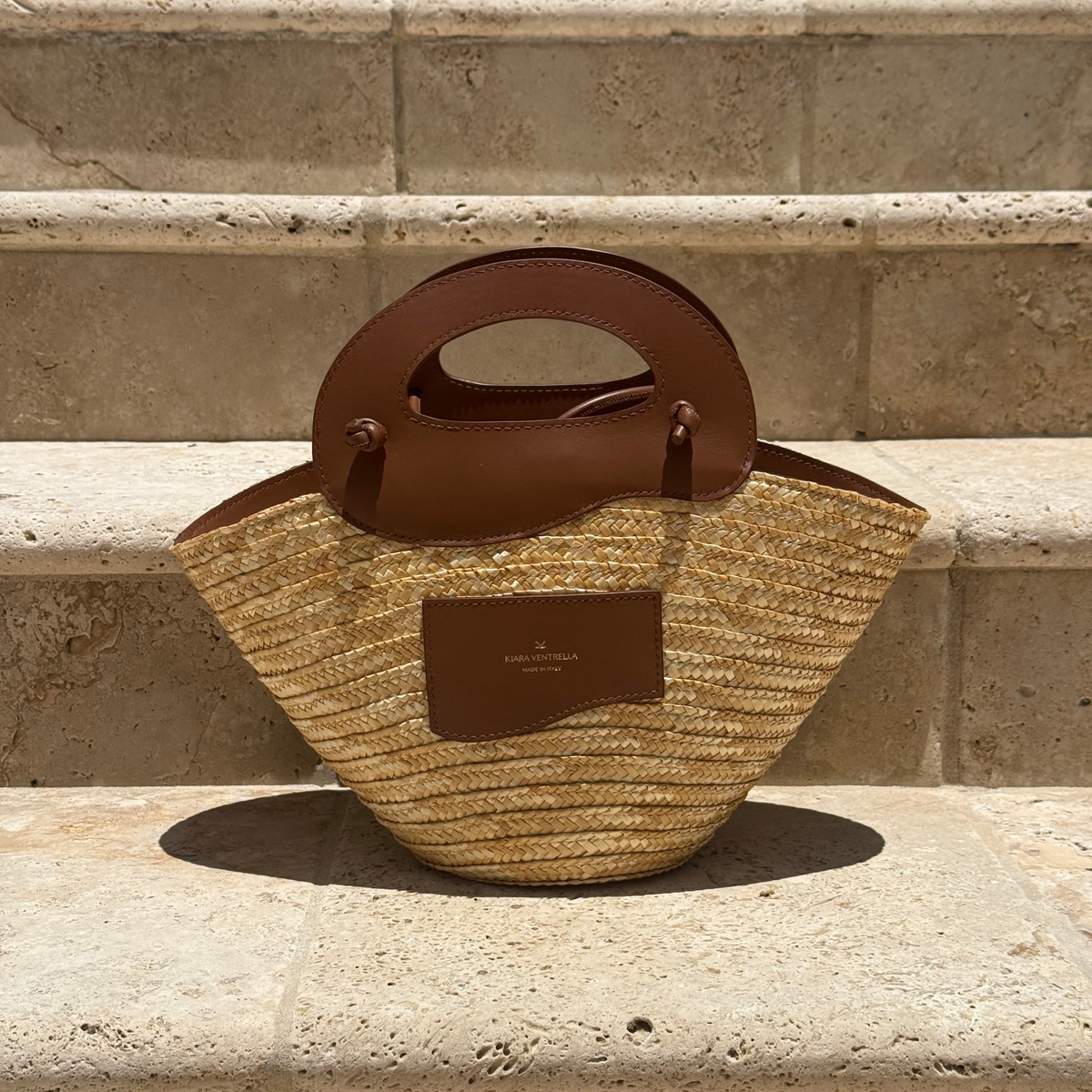 Lifestyle: Marea Straw Bag Small, Smooth Brown Leather (Chestnut),  Leather Wave handles. Lifestyle Outdoor Limestone Steps.
